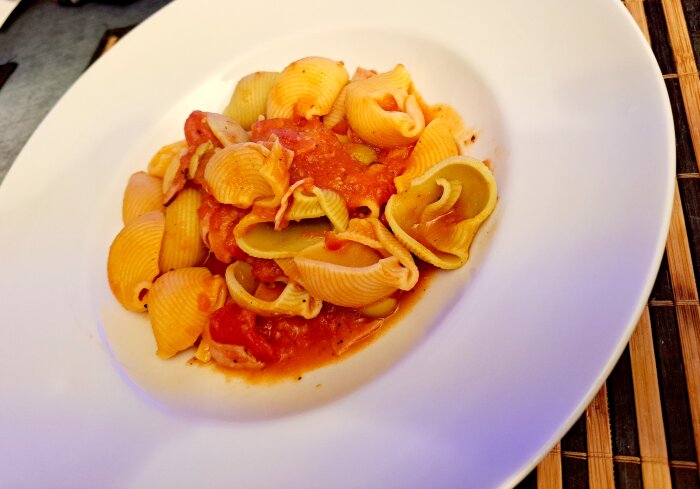 Fusilli-pasta med tomatsås serverad på en vit tallrik, liggande på en bordstablett.