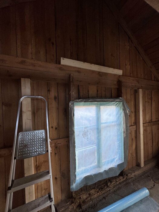 Vägg med förstärkta reglar i en äldre byggnad, plasttäckta fönster och stege för arbete med limträbalkar vid taköppning mot nock.