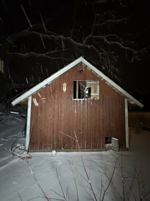 Fasaden av ett rött träslagertorp från tidigt 1900-tal, lätt snötäckt med en fågelholk monterad på väggen.