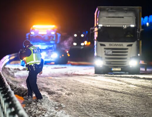 Polis stoppar lastbil på snötäckt väg på natten med blåljus från polisbil och bogseringsfordon i bakgrunden.