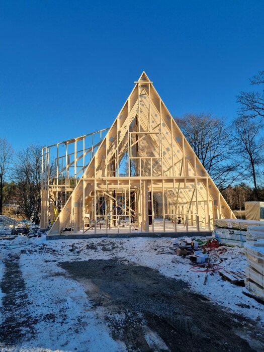 Bygge av ett hus med trekantig takstruktur och synliga träreglar; omgiven av snö, tydlig arkitektur i vardagsrummet.