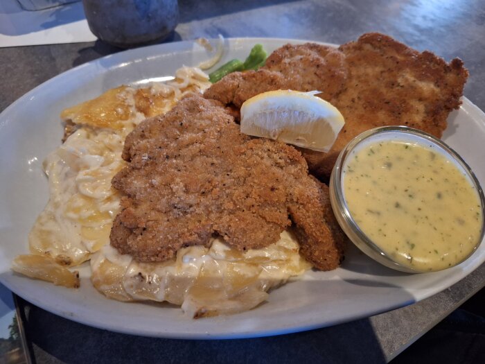 Schnitzel med potatisgratäng, citron och bearnaisesås på en tallrik.