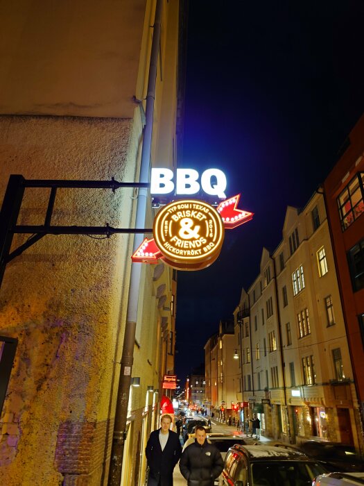 Neonskylt för BBQ-restaurang på en stadsgata i nattbelysning.