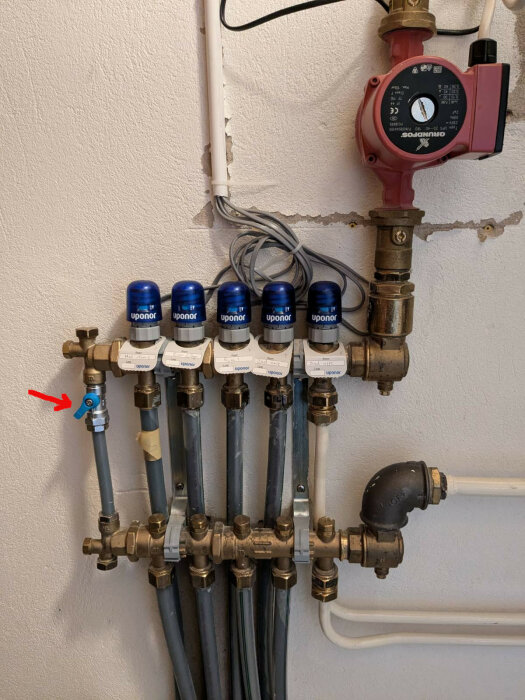 Bild på ljusblå ventil bredvid Uponor-rör i ett värme- och golvvärmesystem, bredvid en röd Grundfos-cirkulationspump.