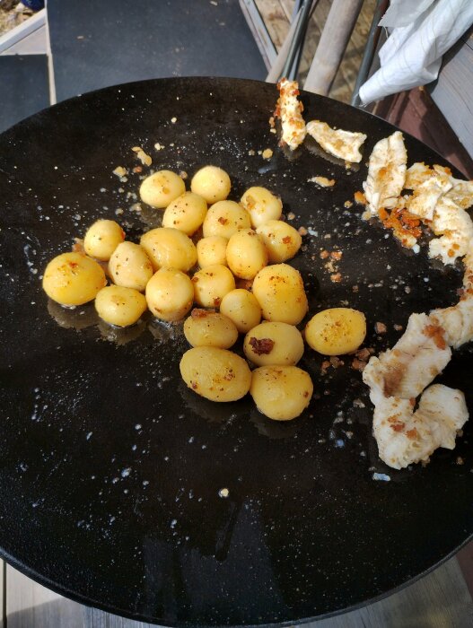 Kolstålspanna med stekta potatisbollar och fiskbitar, visar matlagning utomhus på en murrika.