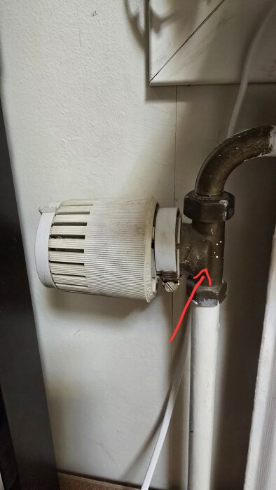 Danfoss RAV 34mm ventil med en röd pil som pekar på anslutningen, monterad på ett värmeelement vid en vägg.