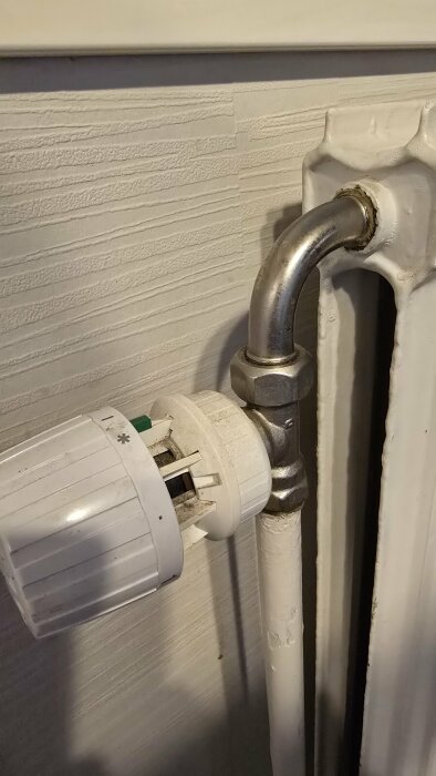 Närbild på ett Danfoss RAV 34 mm termostatventilhuvud installerat på ett vitt element och ansluten via en metallrörledning.