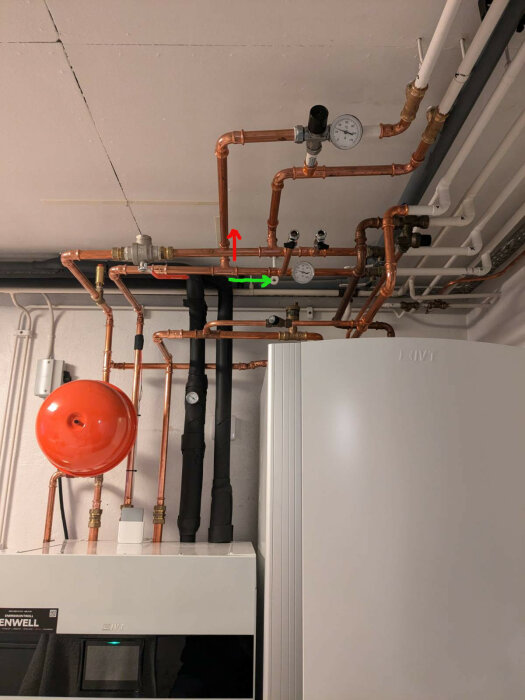 Värmepump med kopparrörsystem, manometer och röd expansionstank placerade i ett pannrum. Röda och gröna pilar markerar varmvattenflödet.