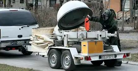 En person i skyddsdräkt undersöker en trailer med en stor, öppen behållare bakom en bil.