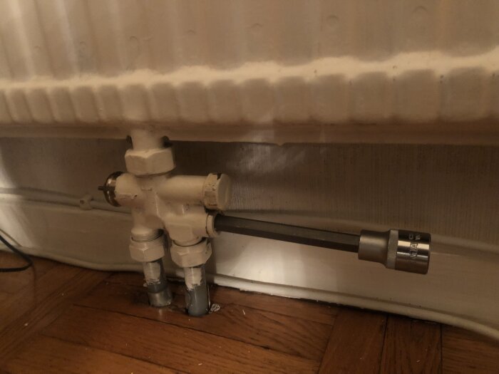 Sexkantsskruv på ett radiatorrör med en fast nyckel på, vid radiator under installation eller reparation i ett bostadsutrymme.