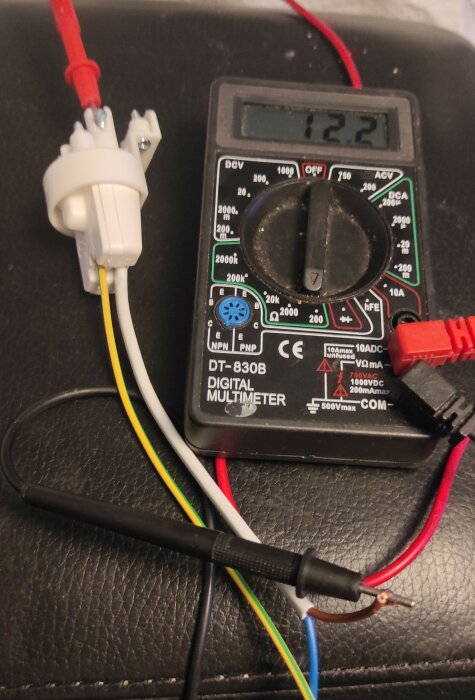 Multimeter DT-830B mäter spänning; kabelanslutningar med olika färger. Avläst värde 12.2V. Används för kontroll av elanslutning.