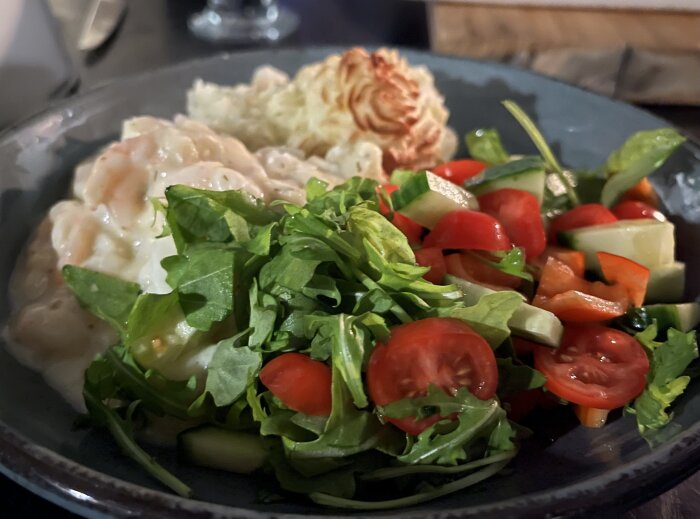 Tallrik med fiskgratäng, rimmad torskrygg, räkor, citron- och dillsås, hemgjort potatismos och sallad med tomat och gurka.