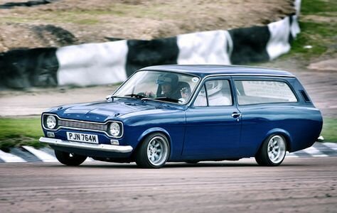 Blå Ford Escort kombi från 1969 på landsväg, två personer synliga inuti bilen.