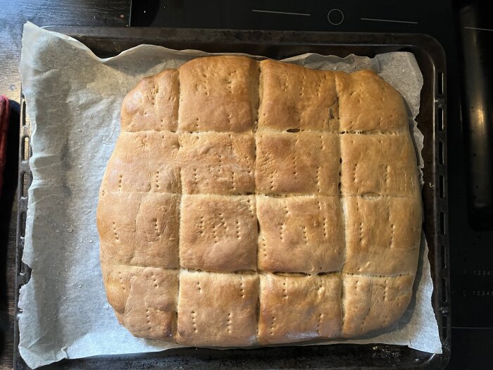 Hemgjort julmustbröd i långpanna, färdiggräddat och delat i rutor, ligger på bakplåtspapper på en ugnsplåt.