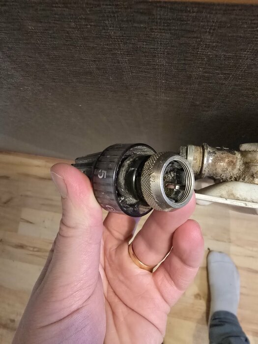 Närbild av en hand som håller en radiatorventil med en felaktig M28 adapter, troligtvis kopplad till ett Tado termostatproblem.