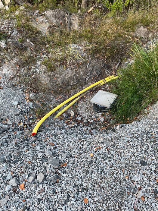 Grop i marken omgiven av grus, med gula elkablar och en kvadratisk betongplatta bredvid grönt gräs.