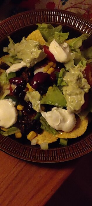Taco tallrik med sallad, majs, bönor, guacamole och gräddfil på ett brunt fat.