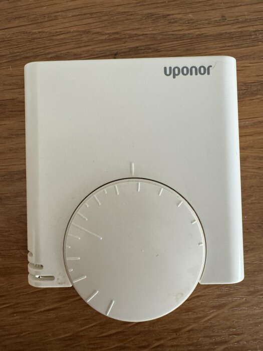 Vit termostat med ratt på en träyta, märkt "Uponor".