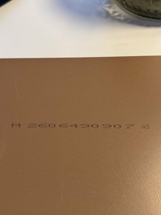 Närbild av ett brungult golv med en svart tryckt kod: "M 2605490307 A3".