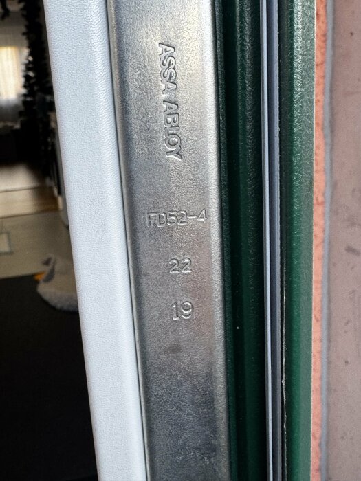 Närbild på en dörrkarm med metallplatta märkt "ASSA ABLOY" och siffrorna "FD52-4", "22" och "19".