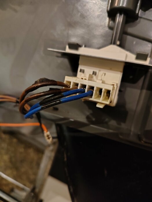 Brun och blå kabel ansluten till vit kontaktdon monterad på en apparat, med en svart och en orange kabel synlig i bakgrunden.