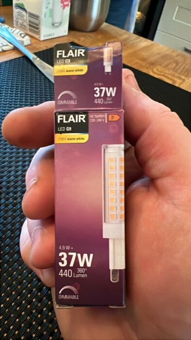 Hand håller förpackning med en dimbar Flair LED G9-lampa, 37W och 2700K varmvit färg.