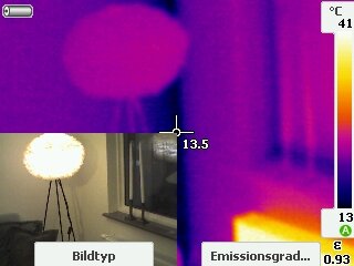 Termisk bild visar en kall yttervägg och ett fönster i en lägenhet med temperaturer runt 13,5°C. Vänster hörn visar en lampa bredvid fönstret.