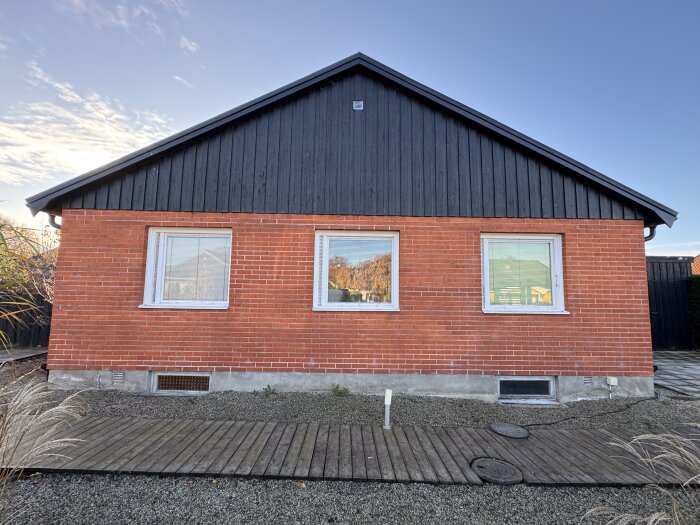 Tegelfasad på ett hus med tre fönster, där arbetet har gjorts för att åtgärda hängande tegel ovanför fönstren.