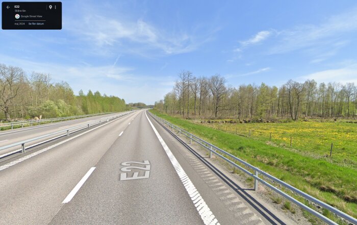 Motorvägen E22 i Skåne före en uppförsbacke, med grönska och träd längs vägen under en klarblå himmel.