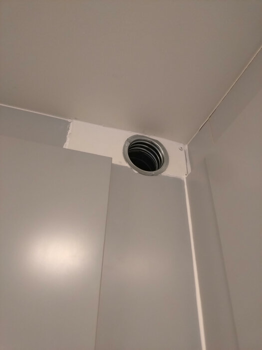 Närbild på kökets hörn med nyligen installerad ventilationsventil och synliga skador på omgivande ytskikt efter arbete utfört av VVS-firma.