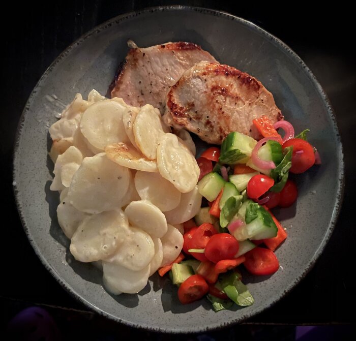 Tallrik med tunna fläskkotletter, potatisgratäng och sallad med picklad rödlök.