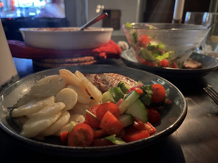 Tunna fläskkotletter, potatisgratäng och sallad med picklad rödlök på en tallrik, med en skål sallad i bakgrunden.