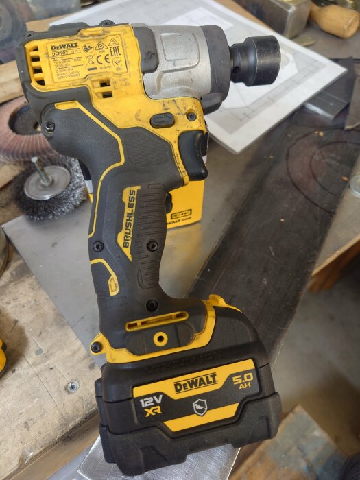 En Dewalt 12V XR batteridriven mutterknackare på ett arbetsbord med verktyg och ritningar i bakgrunden.