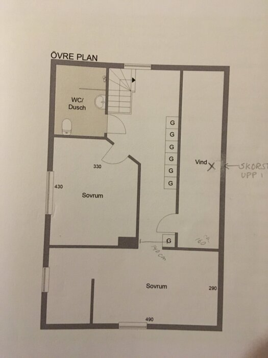 Planlösning över övre plan i ett hus, visar två sovrum, WC/dusch, garderober och vind. Noteringar om mått och placering av skorsten.