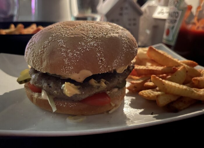 Hamburgare med tomat, gurka, dressing och pommes på tallrik.