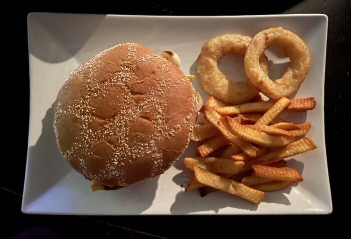 Hamburgare med pommes och lökringar på tallrik.