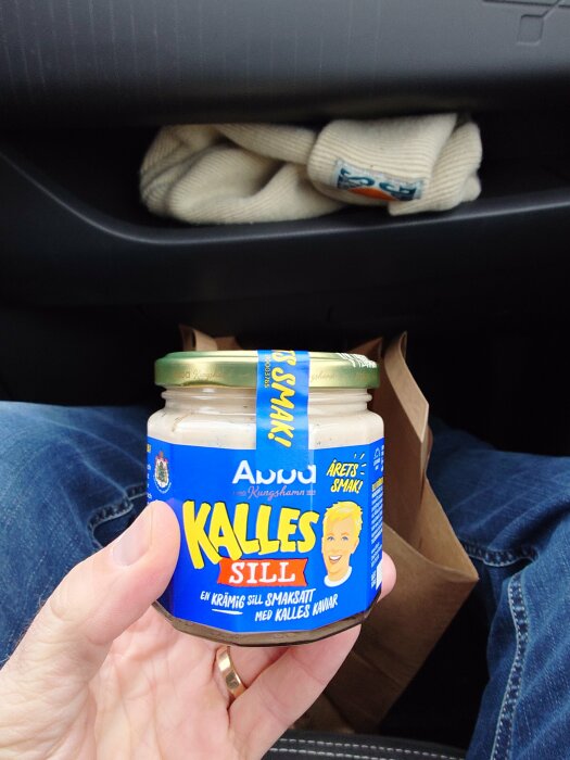 Hand håller en burk Kalles Sill i bilen.