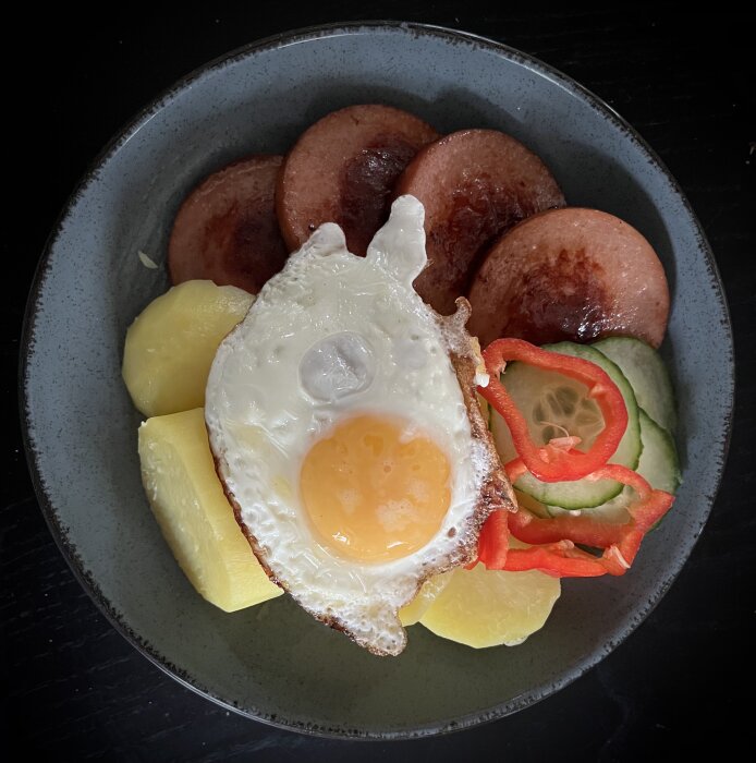 Tallrik med stekt ägg, potatis, korv, gurka och paprika.