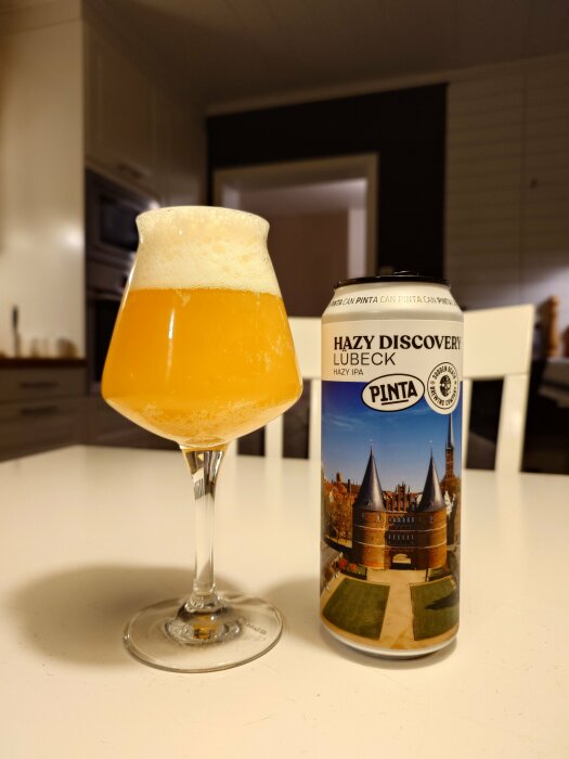 Ett glas öl med skumhuvud bredvid en burk Hazy Discovery Lübeck Hazy IPA av märket Sudden Death på ett bord.