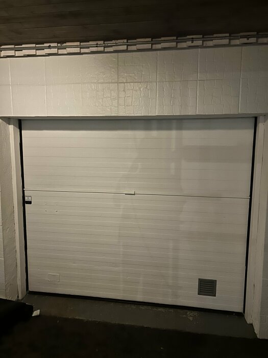 Garageport monterad i huskropp med vit kakelliknande finish, diskussion om installation av spotlights i ovanliggande betong.