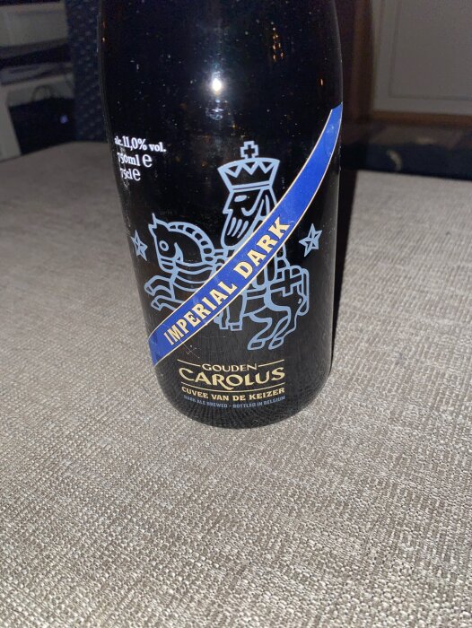 Flaska med etikett för Gouden Carolus Imperial Dark, 11% vol, Cuvée van de Keizer, bryggd i Belgien, placerad på ett bord.