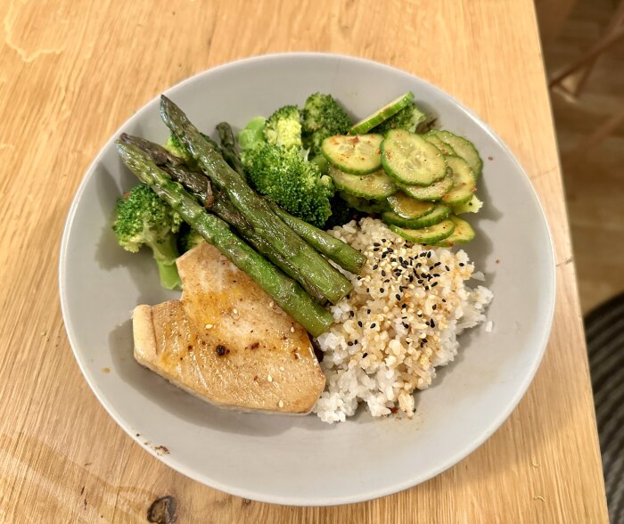 Tallrik med tonfisk, ris med sesamfrön, sparris, broccoli och skivad gurka.