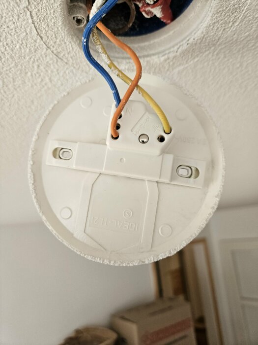 Elektrisk kopplingsplatta i tak med blå, orange och gul kabel ansluten.