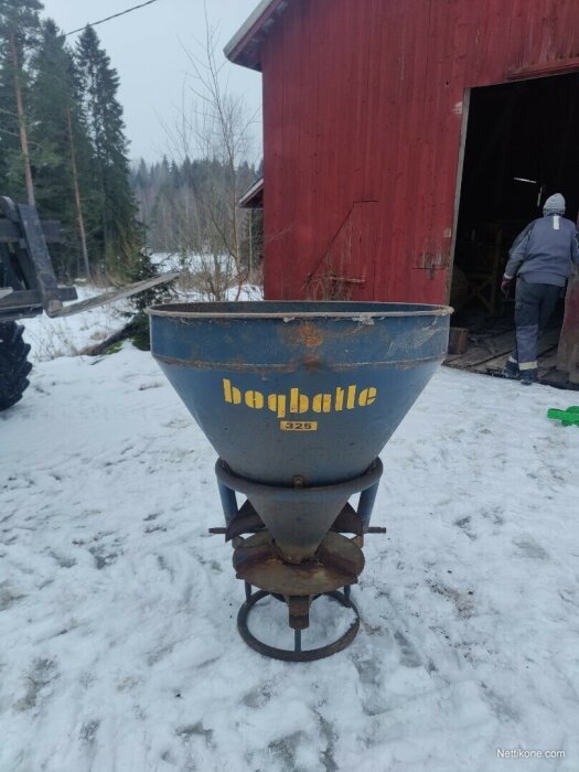 En Bøgballe-spridare står utanför en röd byggnad på en snötäckt yta med skog i bakgrunden.