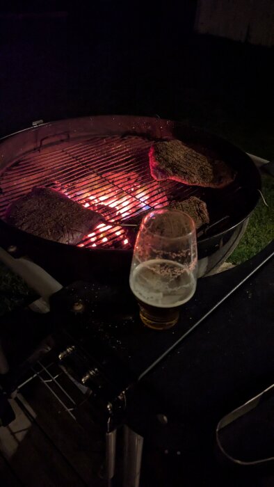 Grill med glödande kol och ett glas öl från Brooklyn Brewery East IPA på kvällen.