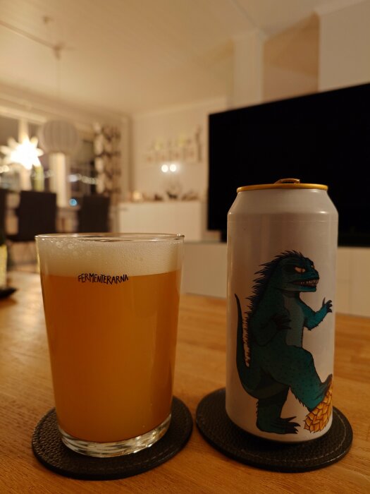 Ett glas med skummande öl och en burk med illustration av ett monstrum på ett bord i ett vardagsrum.