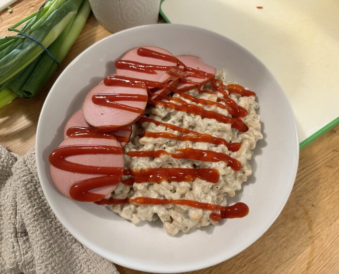 Tallrik med stuvade makaroner och skivor av basturökt korv, dekorerade med ketchup.