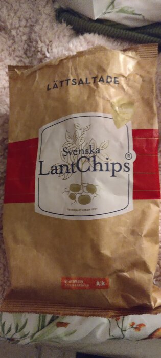 Påsen med Svenska LantChips, lättsaltade, visas på en mjuk yta med blommönster i bakgrunden.