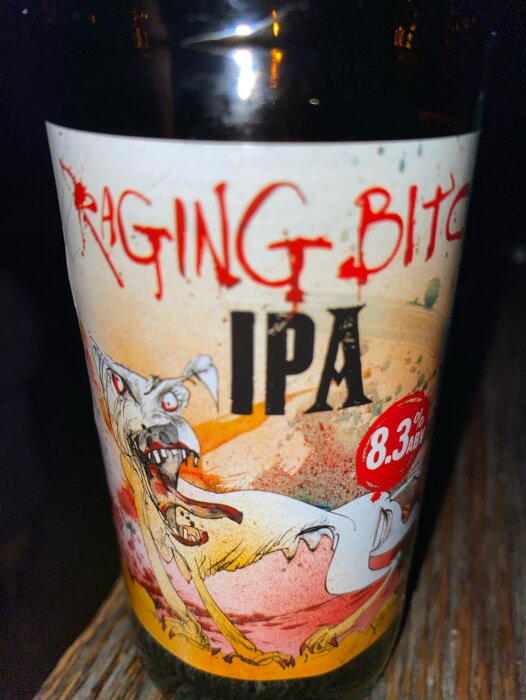 Etikett på ölflaska med texten "Raging Bitch IPA" och en illustration av en aggressiv hund. Alkoholhalt 8.3%.