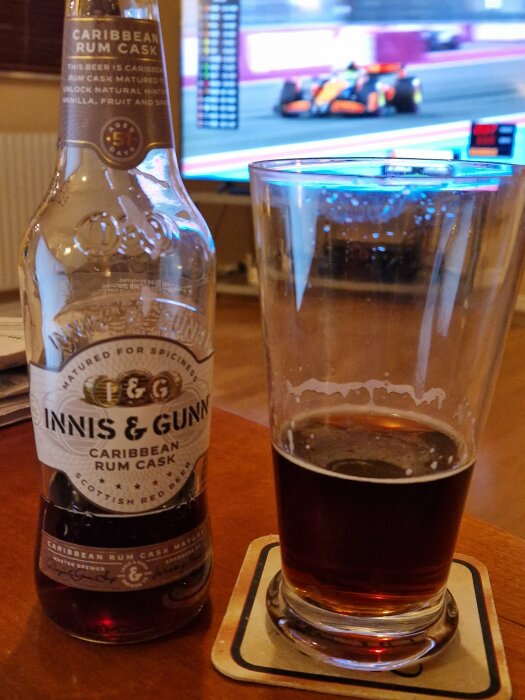 Ölflaska och glas med Innis & Gunn framför en TV som visar Formel 1-lopp, på ett träbord.